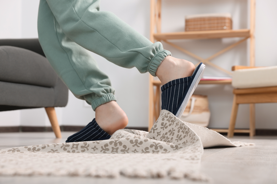 Person tripping over a lifted rug in a home whilst wearing slippers.